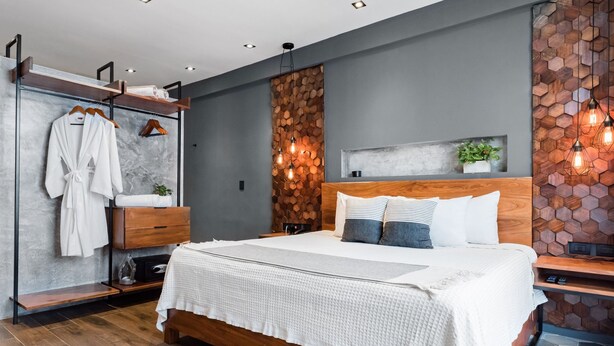 Une chambre moderne avec un grand lit, une tête de lit en bois et une armoire intégrée dotée d’un miroir.