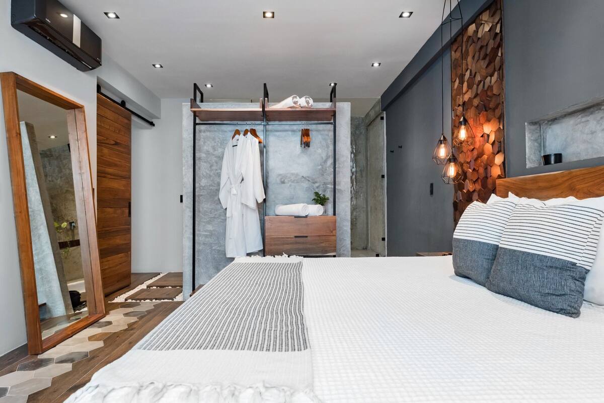 Een moderne slaapkamer met een groot bed, een houten garderobe, een spiegel en een ingebouwde bank met opbergruimte.