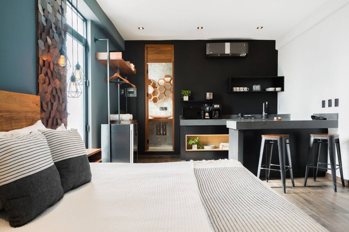 Een moderne slaapkamer met een groot bed, een houten hoofdbord en uitzicht op een keuken met een bar.