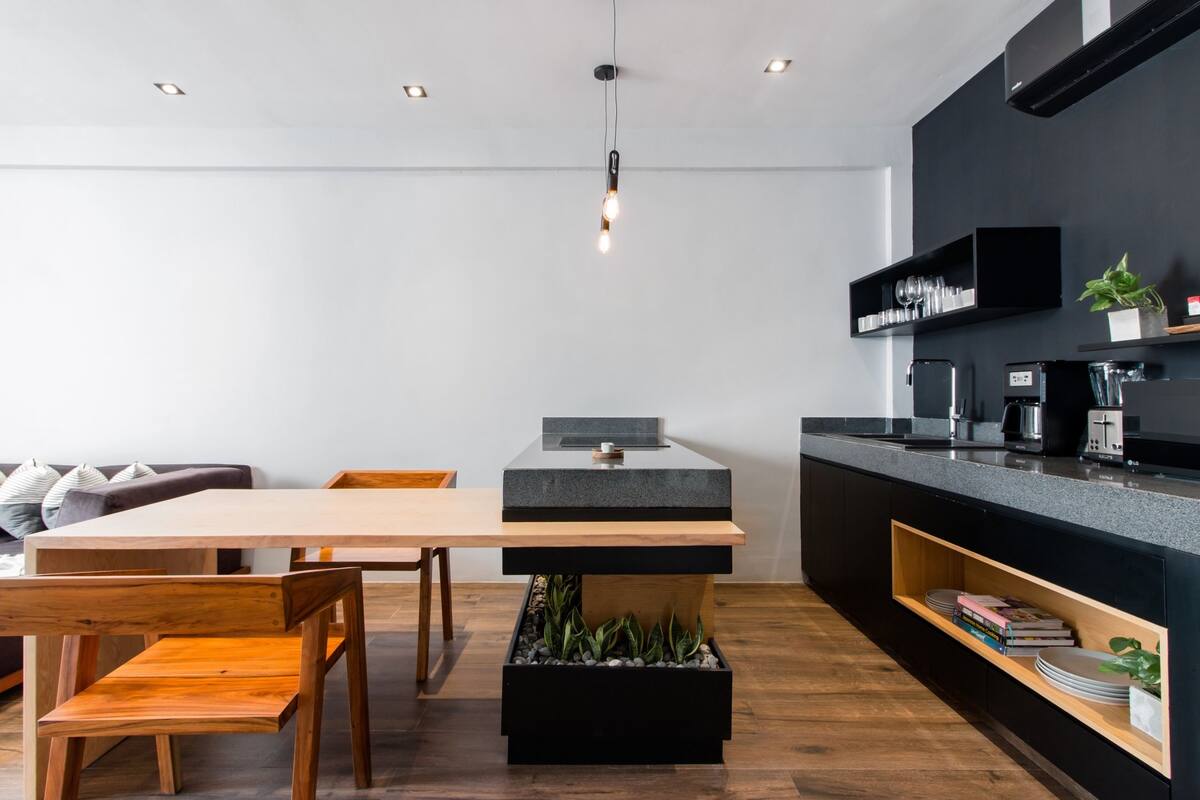 Een moderne keuken met een houten eettafel, zwarte kastjes en een inbouwkookeiland met aanrecht.
