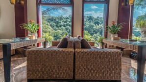 A seating area with wicker furniture and a view of a lush forest through arched windows. - Siqi Inn (Baoshan)