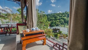 A room with a traditional wooden table set with teapots and cups, a sofa, and a view of a lush green landscape through large windows. - Siqi Inn (Baoshan)