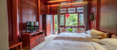 A traditional room with two beds, a television on a wooden cabinet, and a view of greenery outside.