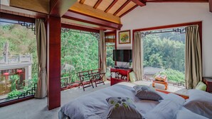 A bedroom with a large bed, a TV, a small table, and a balcony with a view of greenery. - Siqi Inn (Baoshan)