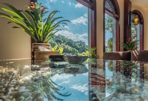 Une table en verre offrant une vue dégagée sur un jardin luxuriant et sur une structure en bois, visible à travers le verre.