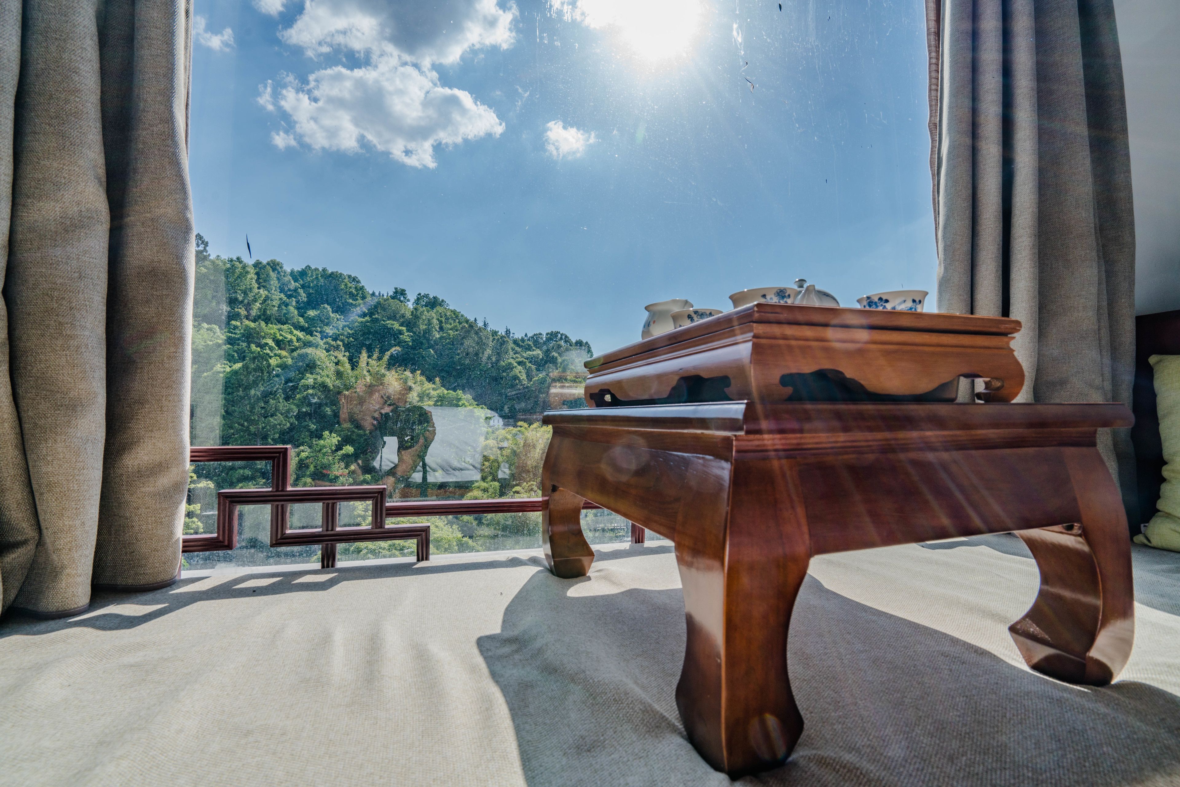 A wooden table with a view of a green landscape through a window.
