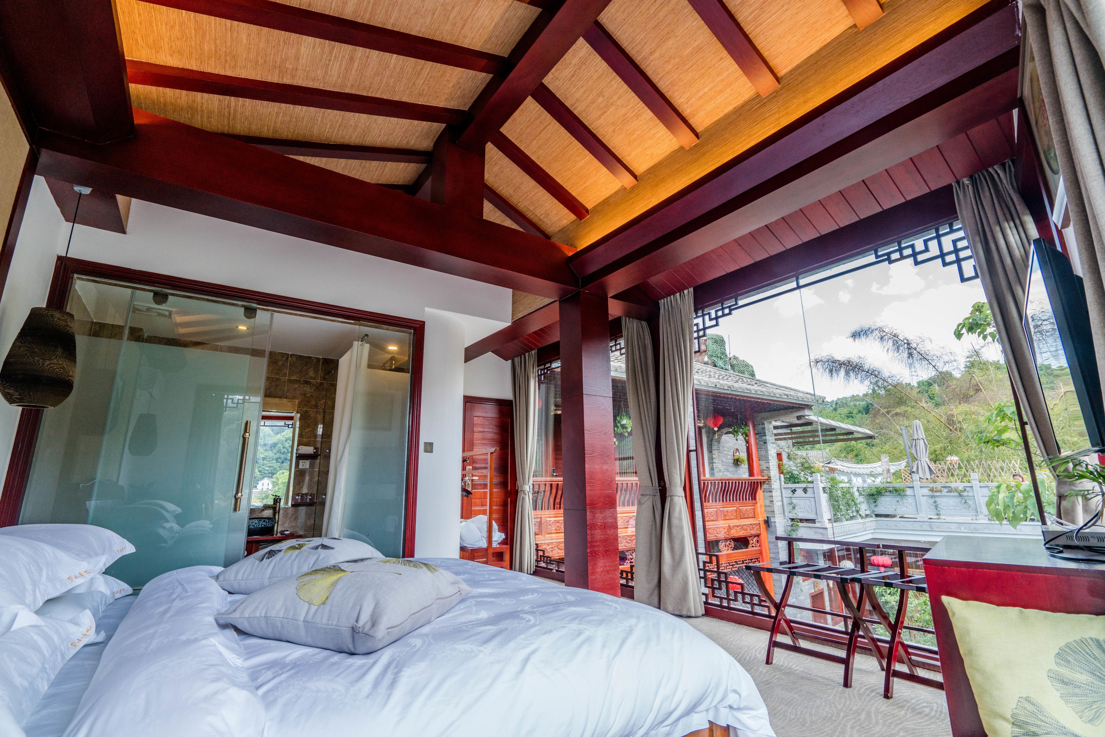 A hotel room with a large bed, a balcony with a table and chairs, and a view of traditional architecture.