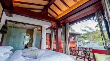 A hotel room with a large bed, a balcony with a table and chairs, and a view of traditional architecture.