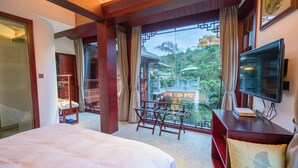 A hotel room with a large bed, a TV, a desk, and a balcony with a view of traditional architecture and greenery. - Siqi Inn (Baoshan)