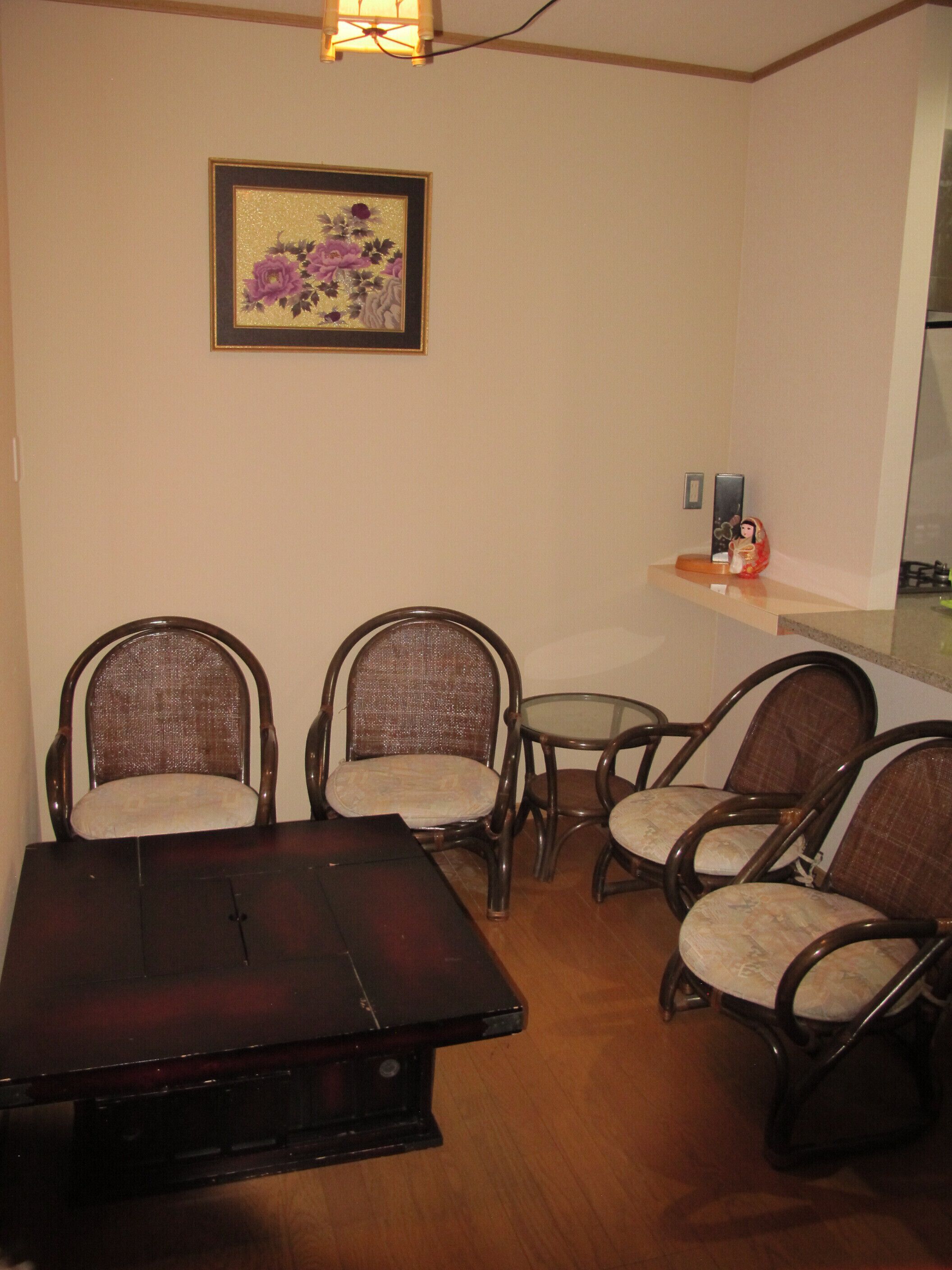 Uma área de refeições com uma mesa de madeira escura e quatro cadeiras de vime com assentos acolchoados. Uma obra de arte floral emoldurada está pendurada na parede acima da mesa.