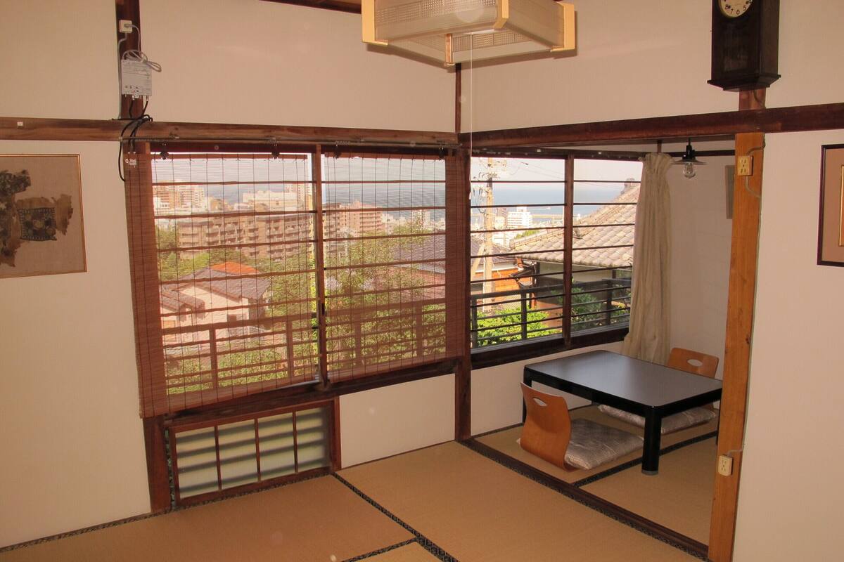 Una habitación japonesa tradicional con suelo de tatami, una mesita baja y vistas a la ciudad a través de amplios ventanales.