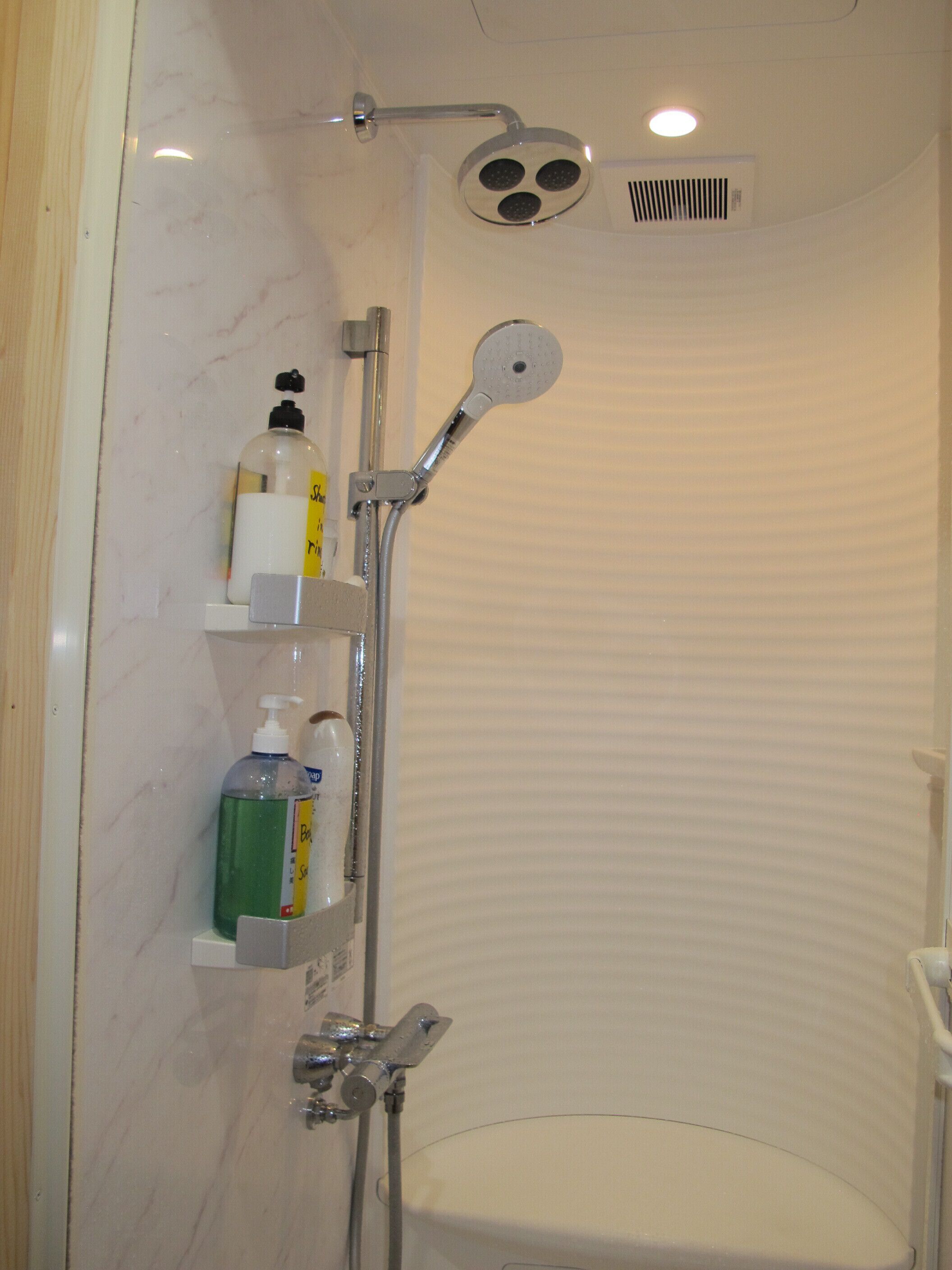 A shower with a handheld showerhead, a wall-mounted hand dryer, and a shelf with toiletries.