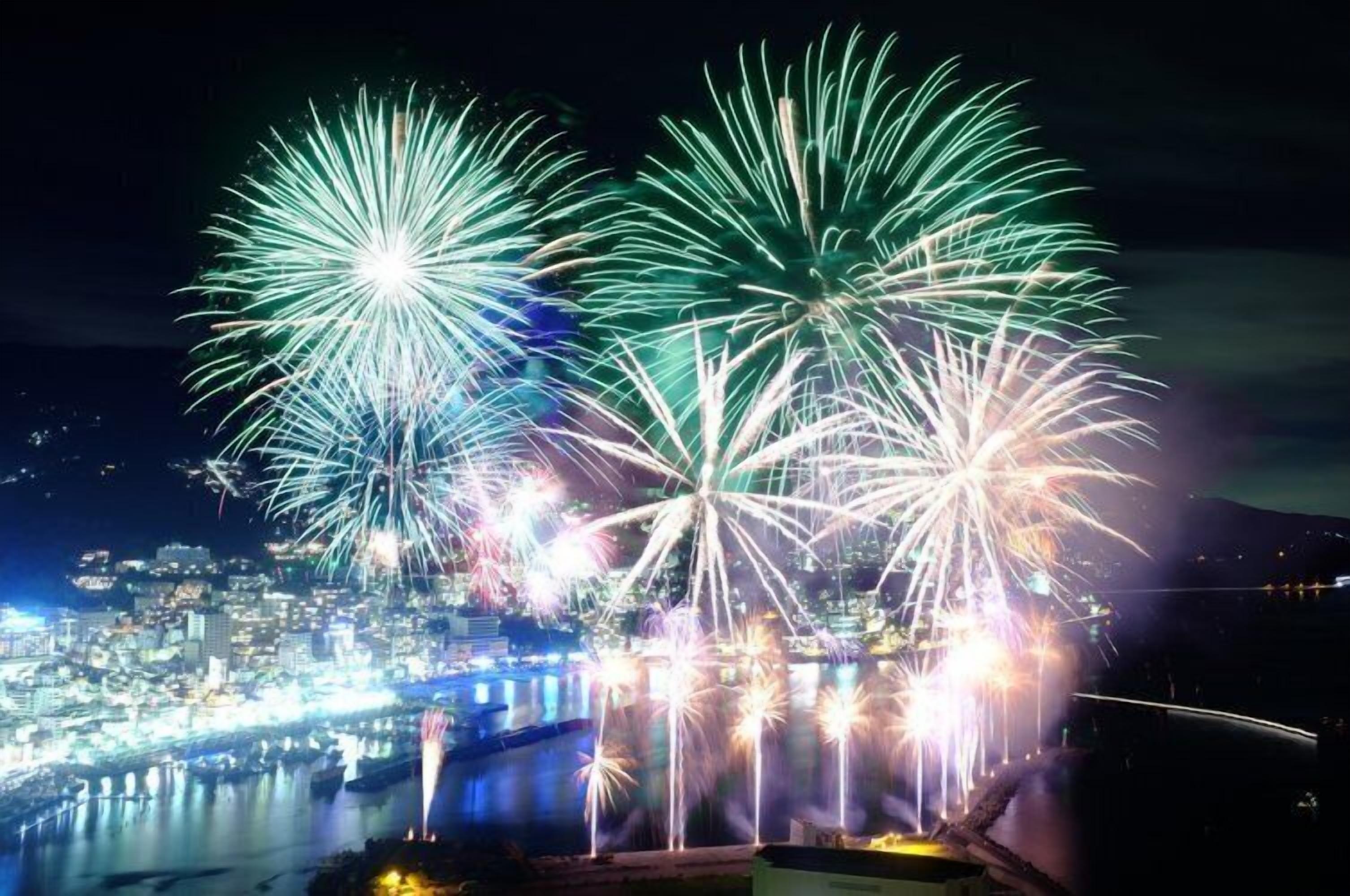 A nighttime cityscape with fireworks over a body of water and a bridge.
