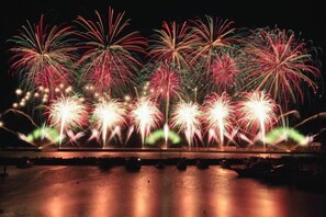 A nighttime fireworks display over a body of water with reflections on the surface.