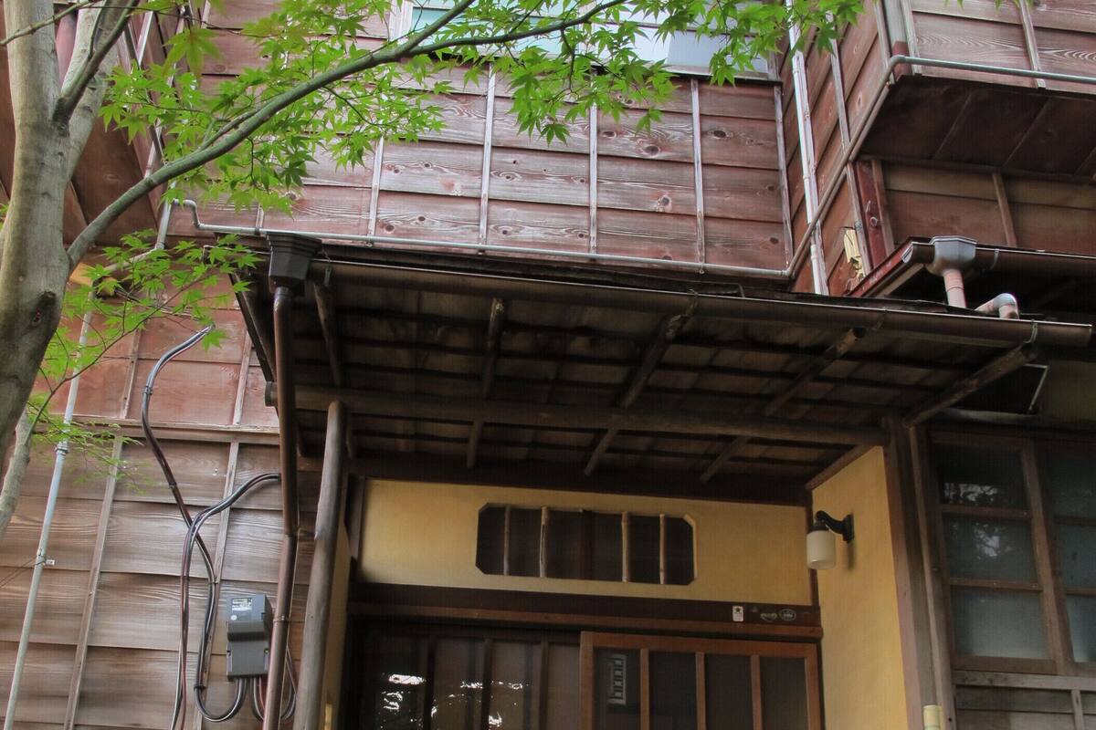 Un edificio de madera tradicional con un acceso de baldosas, una puerta de madera y una pequeña zona de porche.