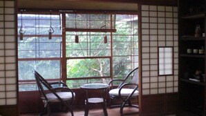 A traditional Japanese room with tatami flooring, a low table, two chairs, and a large window with a view of greenery. - Atami Ikkyuan (Atami)