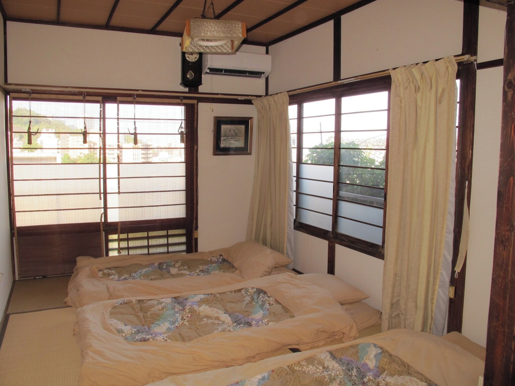 Una habitación japonesa tradicional con suelo de tatami, dos camas con ropa de cama floral, un reloj y un cuadro en la pared.