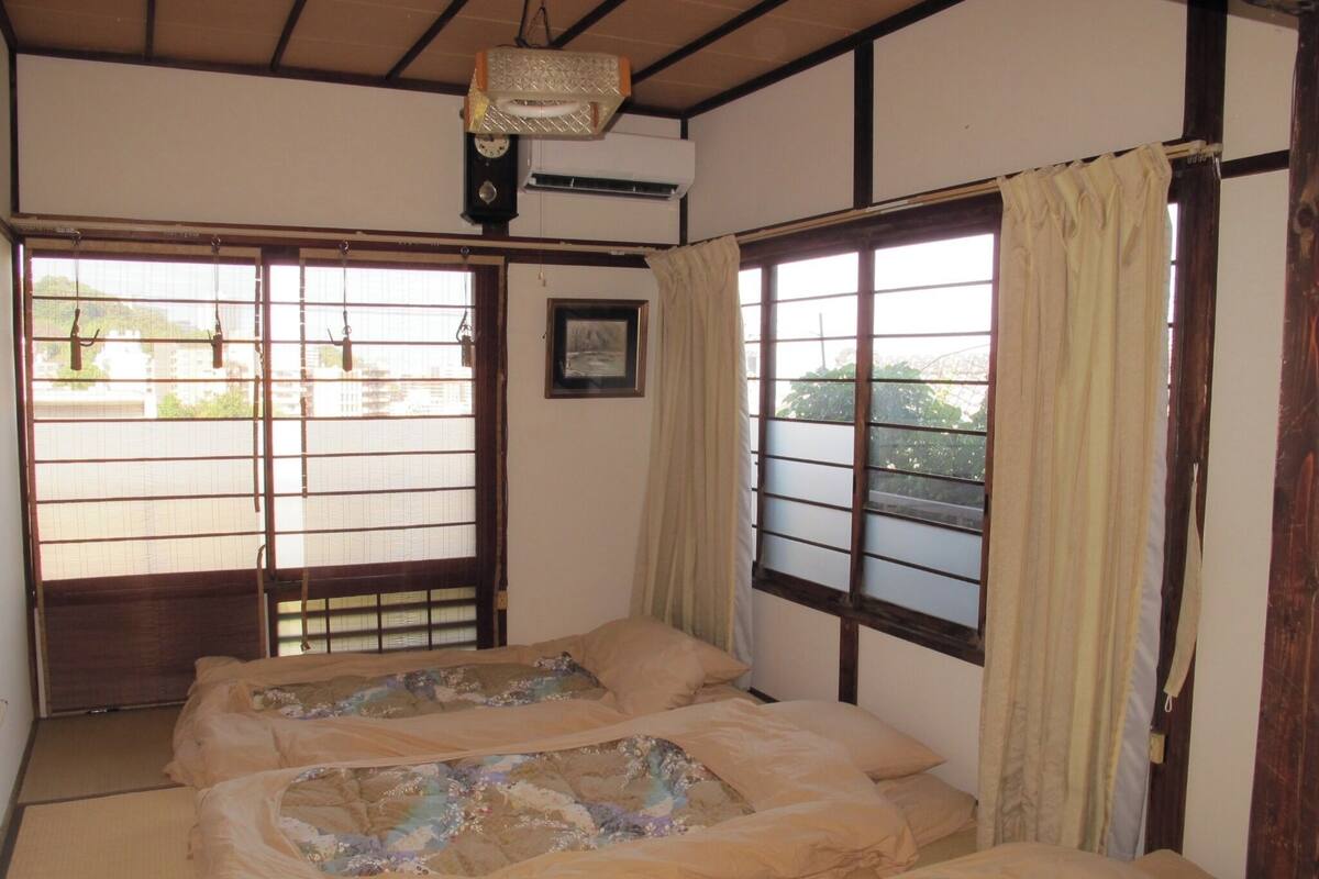 Una habitación japonesa tradicional con suelo de tatami, dos camas con ropa de cama floral, un reloj y un cuadro en la pared.