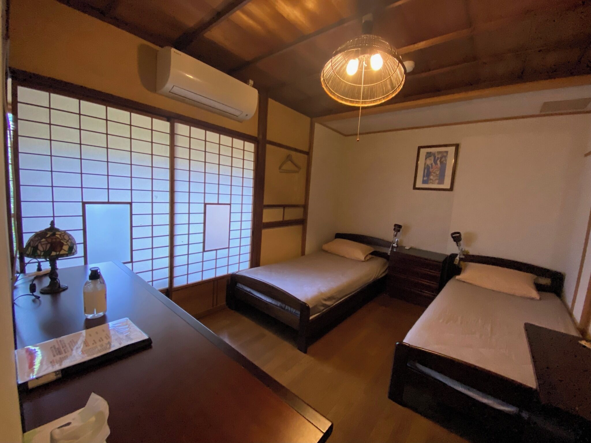 Una habitación tradicional japonesa con suelo de tatami, una mesa baja con una lámpara y una cama con cabecera de madera.