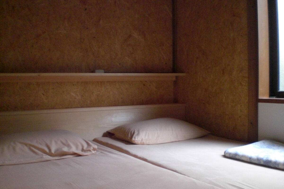 Una cama individual con dos almohadas en una habitación con paredes de madera y un ventanal.