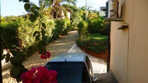 A narrow cobblestone path flanked by lush greenery and a white car parked on the side. - Charming House With Stunning Views (Paraty)