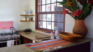 A kitchen with a gas stove, a window with a view, a vase with flowers, and a shelf with kitchen items. - Charming House With Stunning Views (Paraty)