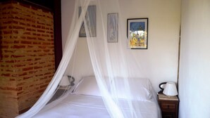 A bed with white bedding and a mosquito net, a nightstand with a lamp, and a brick wall. - Charming House With Stunning Views (Paraty)