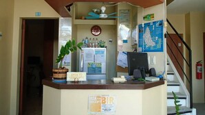 Ein Empfangsschalter mit einem Schild, das "OPEN TO SERVE YOU!" zeigt, und einem Schild für "ASK FOR RECEIPT". Ein Computer, eine Pflanze und eine Karte sind an der Wand angebracht.