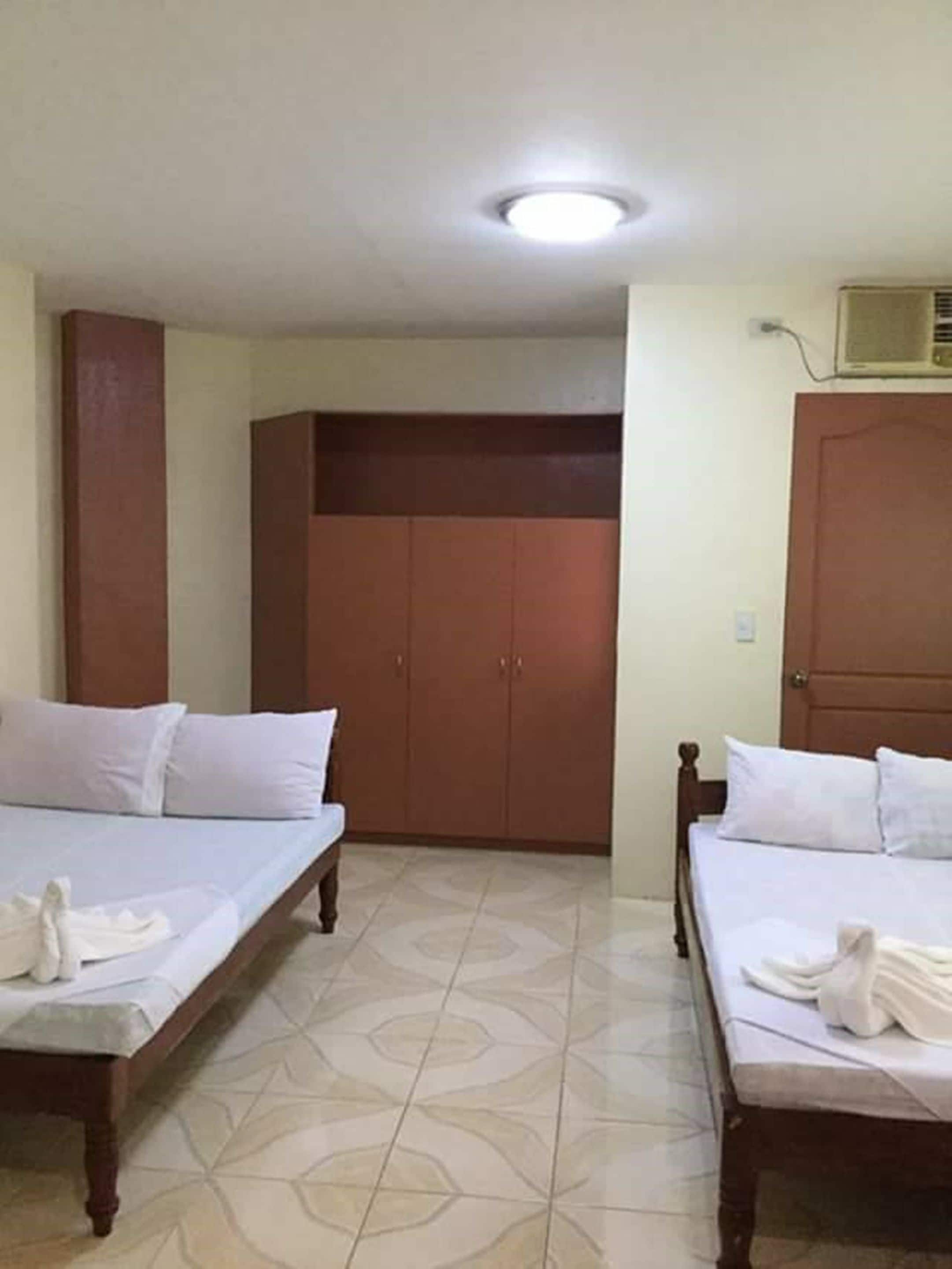 Een hotelkamer met twee enkele bedden, een kledingkast en een plafondventilator.