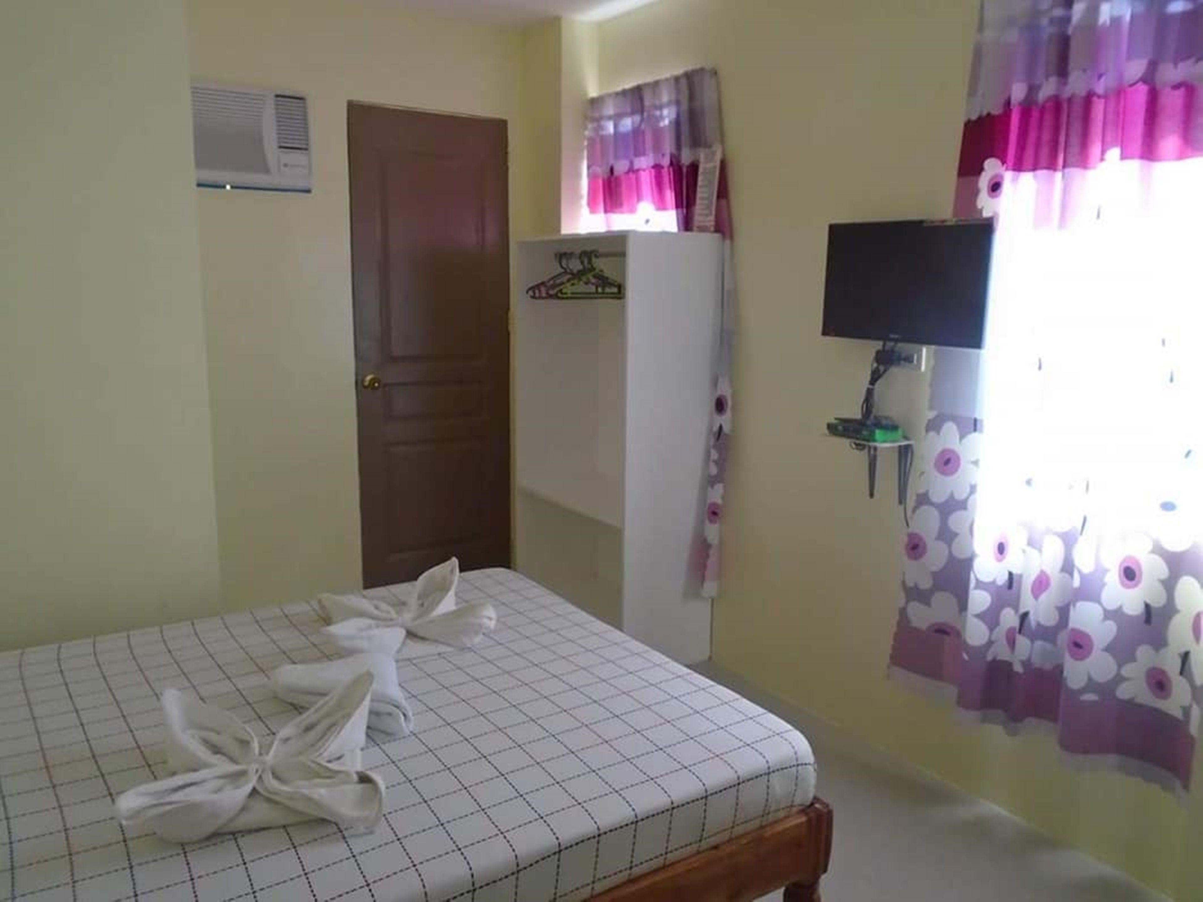 A bedroom with a bed, a wardrobe, a television, and a window with curtains.