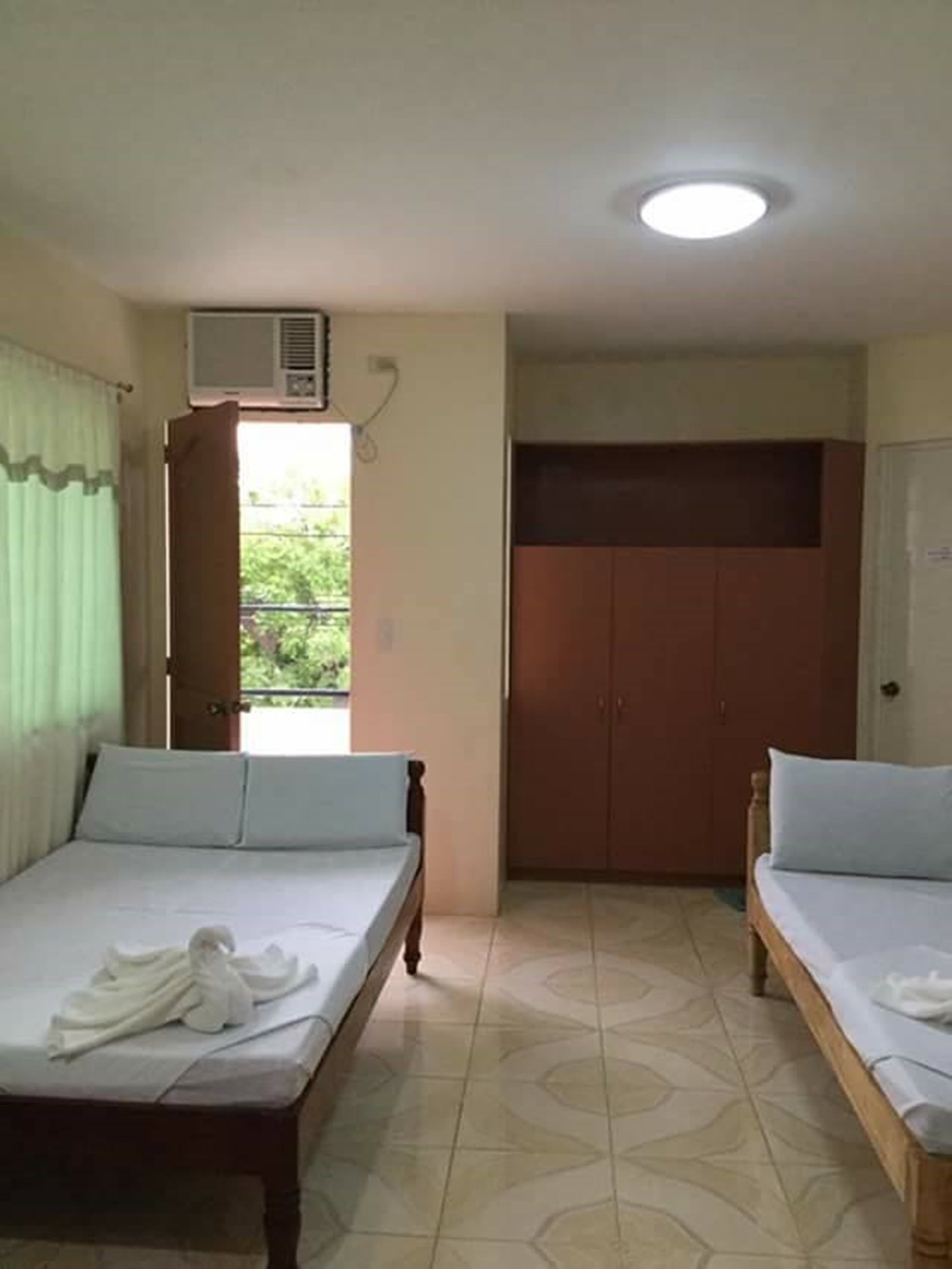 A room with two beds, a wardrobe, and a window with curtains.