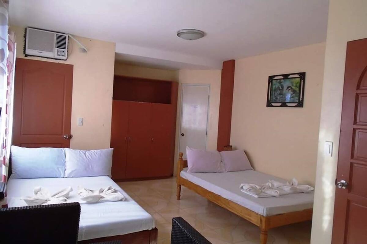 A hotel room with two beds, a wardrobe, a small table, and a ceiling fan.