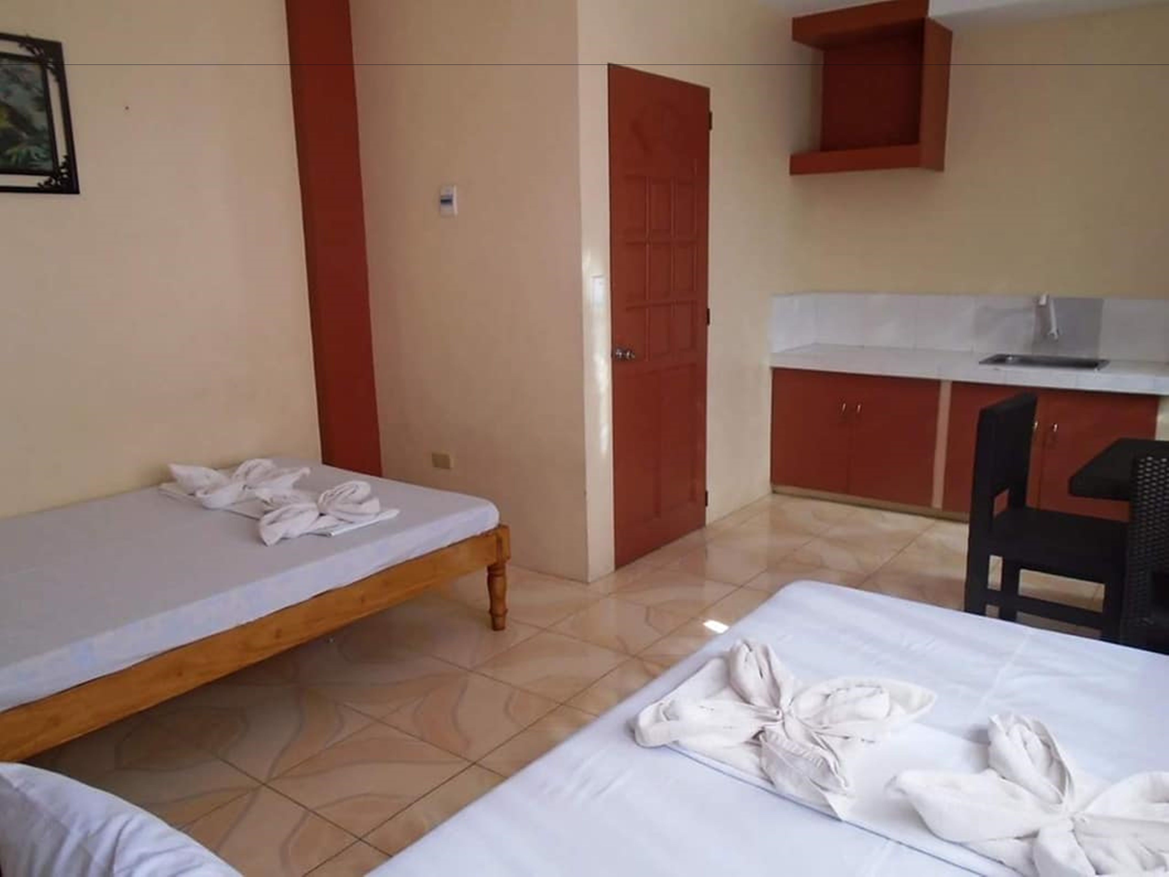 A hotel room with a bed, a chair, a small desk, and a kitchenette.