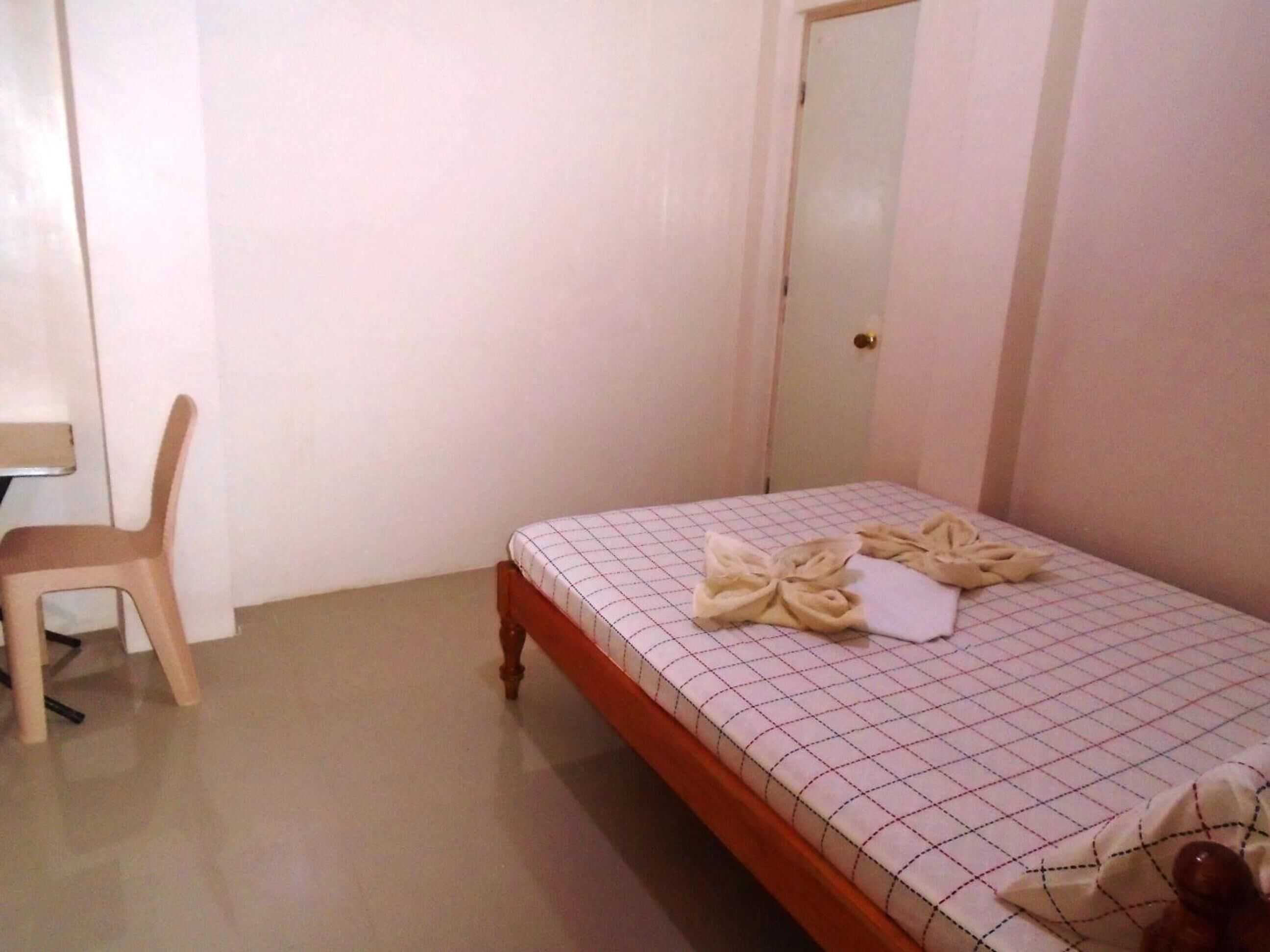 A small, clean room with a single bed, a wooden chair, and a door.