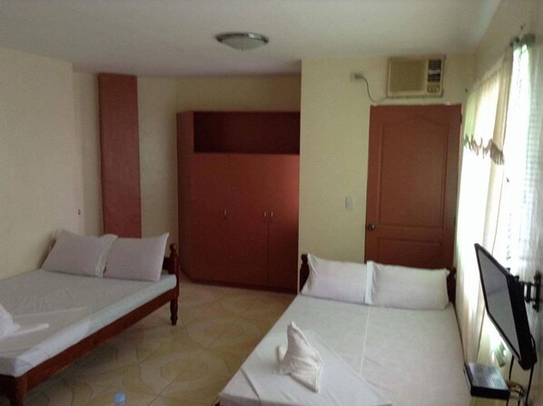 A room with two beds, a wardrobe, and a desk with a computer.