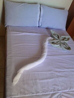 A bed with a white sheet and a towel arranged in a flower shape on the bed.