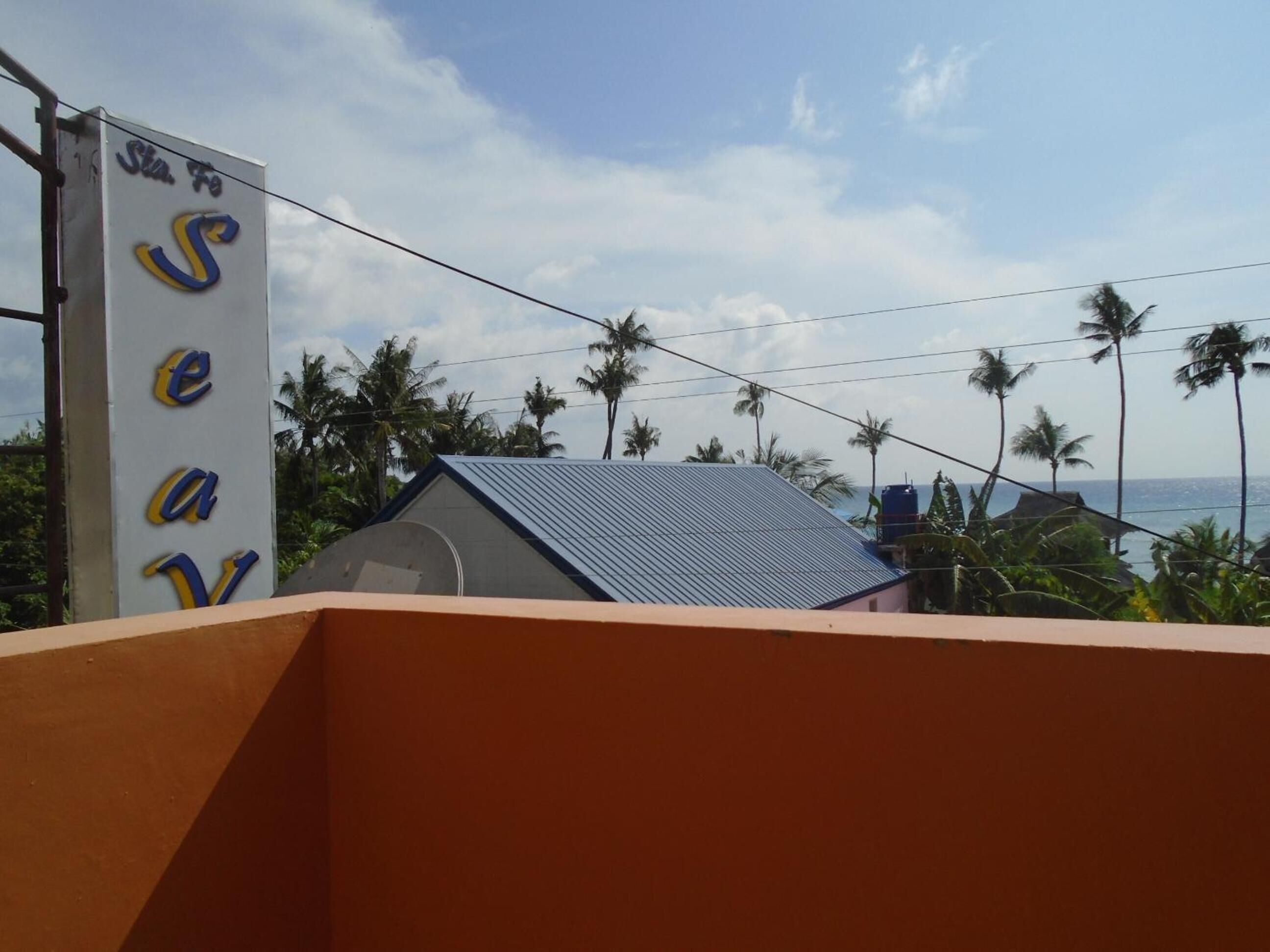 A hotel sign with the name 'Sea' and a view of a building with a blue roof and palm trees in the background.