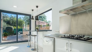 Une cuisine moderne équipée d’une cuisinière à gaz, de meubles en acier inoxydable et d’une grande fenêtre donnant sur un jardin.