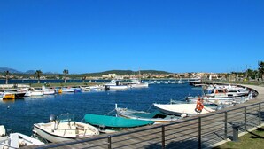 A marina with various boats docked, a clear blue sky, and a distant view of a town with buildings and hills. - Beautiful  villa for 8 people with A/C, private pool, TV and patio (Olbia)