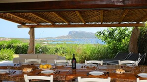 An outdoor dining area with a table set for six, overlooking a scenic view of the sea and mountains. - Beautiful  villa for 8 people with A/C, private pool, TV and patio (Olbia)