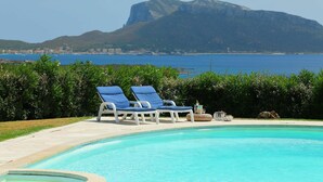 A pool with two blue lounge chairs, a stone edge, and a view of a mountain and sea. - Beautiful  villa for 8 people with A/C, private pool, TV and patio (Olbia)