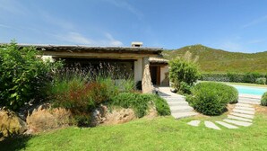 A rustic house with a stone pathway leading to a pool, surrounded by lush greenery and a mountain in the background. - Beautiful  villa for 8 people with A/C, private pool, TV and patio (Olbia)