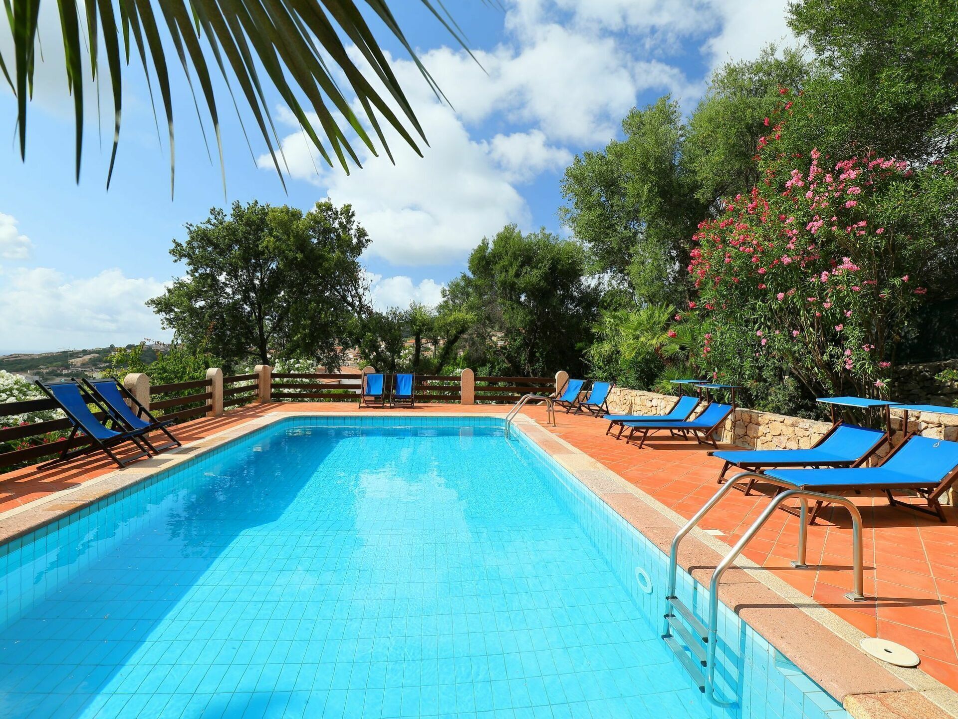 Una piscina con piso de baldosas azules, rodeada de muros de piedra y sillas reclinables azules.