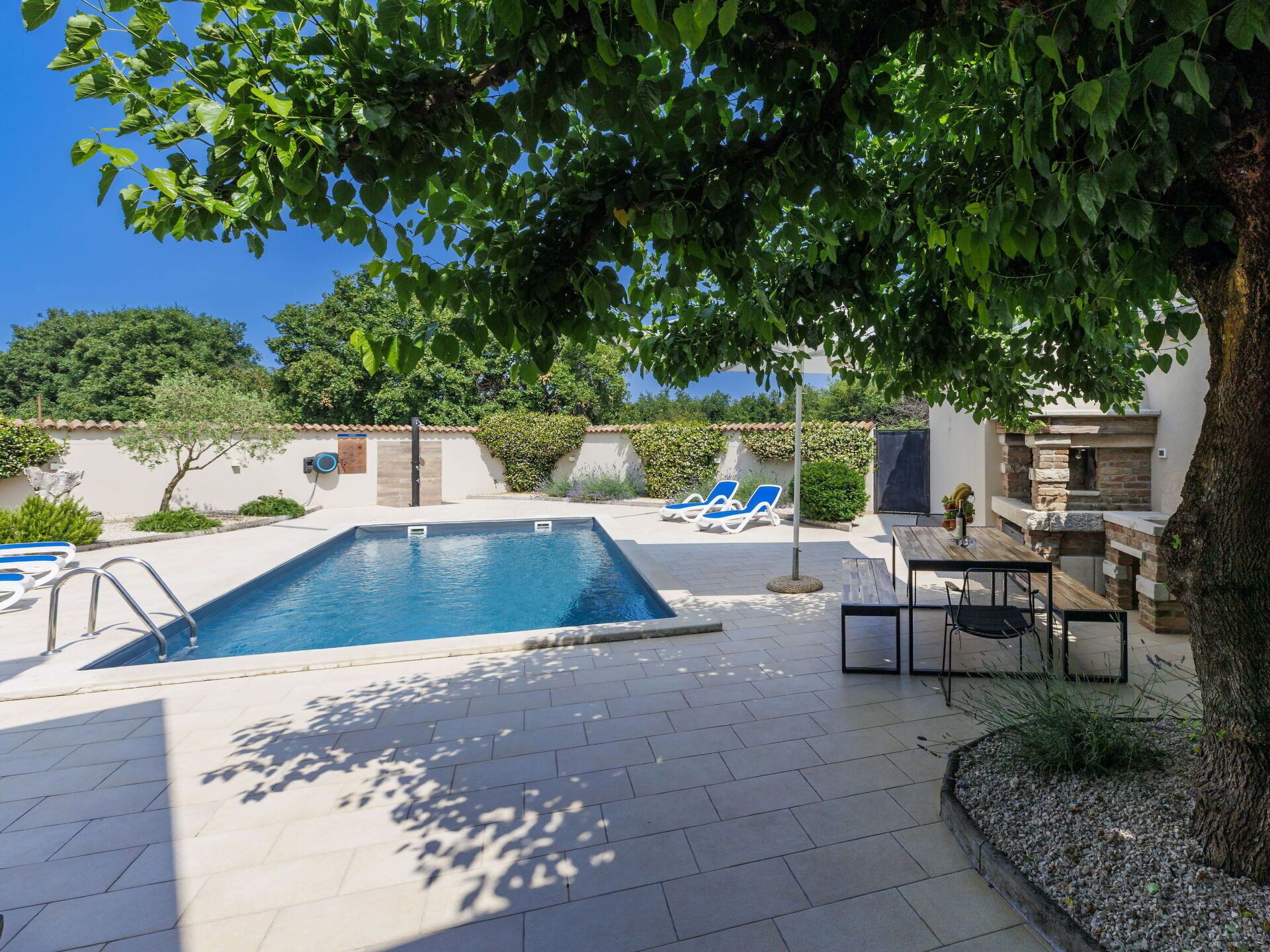 A swimming pool with lounge chairs, a barbecue area, and a pergola providing shade.