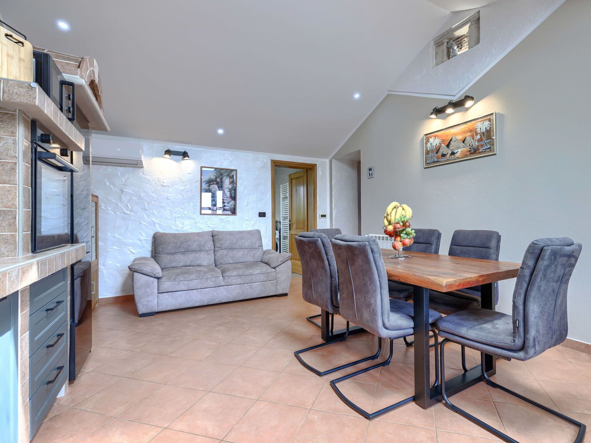 A modern living space with a dining area, a sofa, and a kitchen.