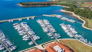 An aerial view of a marina with numerous boats docked, surrounded by greenery and a clear blue sea. - Beautiful  villa for 8 people with A/C, private pool, WIFI, TV and terrace (Umag)