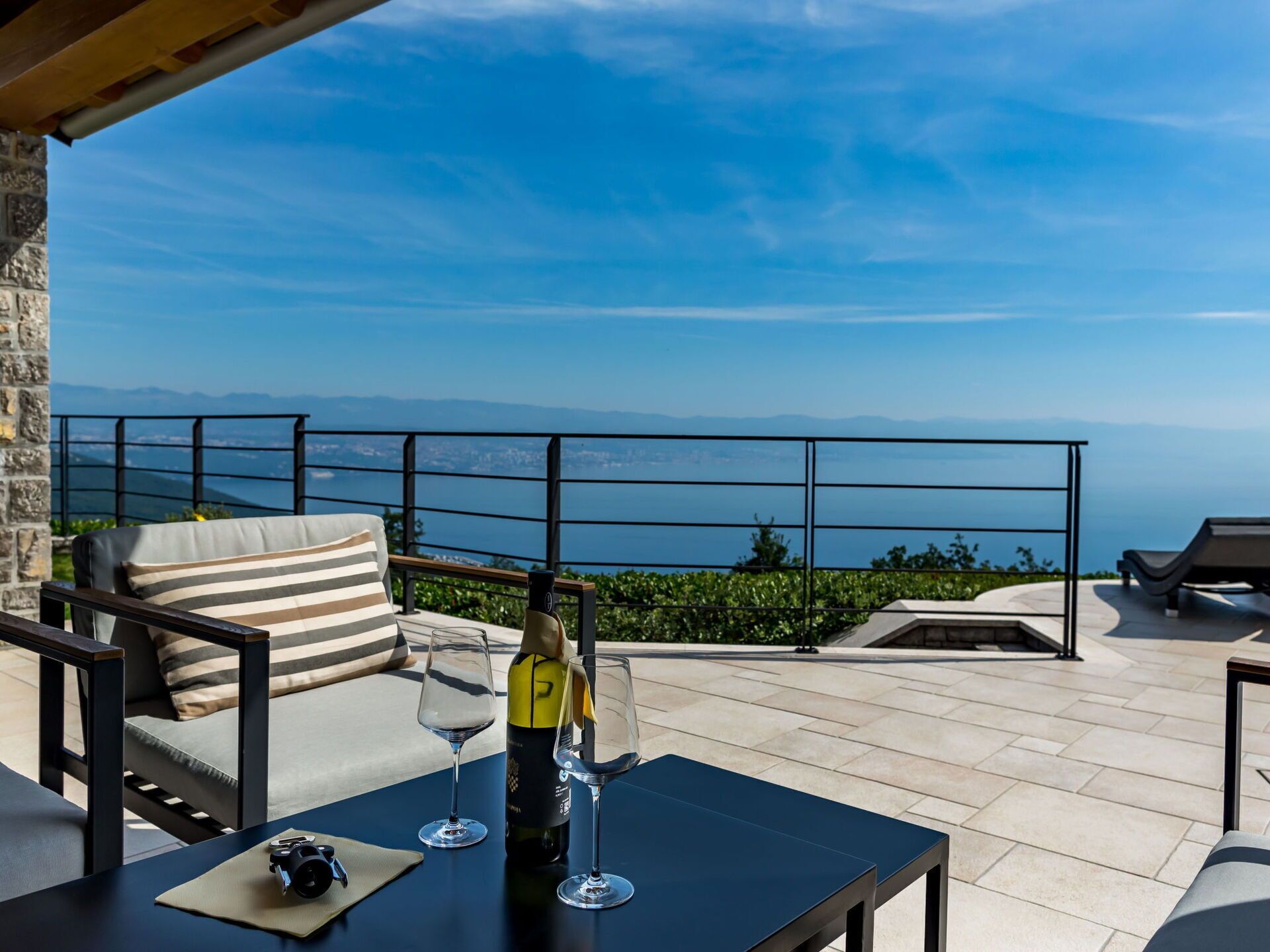 A terrace with a table, chairs, and a bottle of wine.