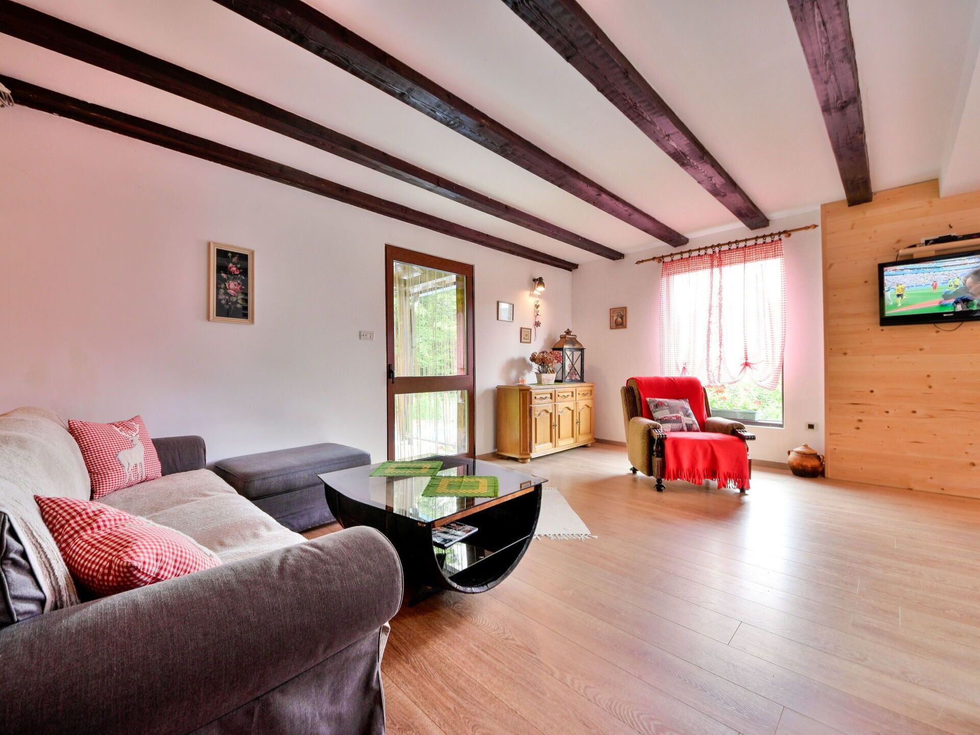 Una sala de estar con un sofá, un sillón rojo, un aparador de madera y un televisor en la pared.