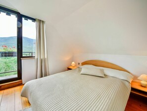 Une chambre à coucher avec un grand lit, une table de chevet, une lampe et une vue sur un paysage montagneux par une grande fenêtre.
