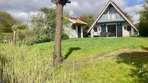 Une maison avec un toit en pente, une cour couverte d’herbe et un grand arbre.
